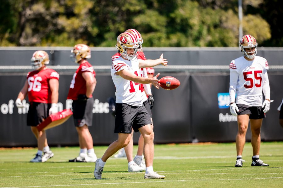 Jack Bouwmeester in a white 49ers practice jersey and gold helmet on the club's practice field, stepping into a punt with the ball dropping from his hand and two teammates in the same practice kit behind him. San Francisco waived Bouwmeester on August 12, 2026, twenty-five days after he signed.