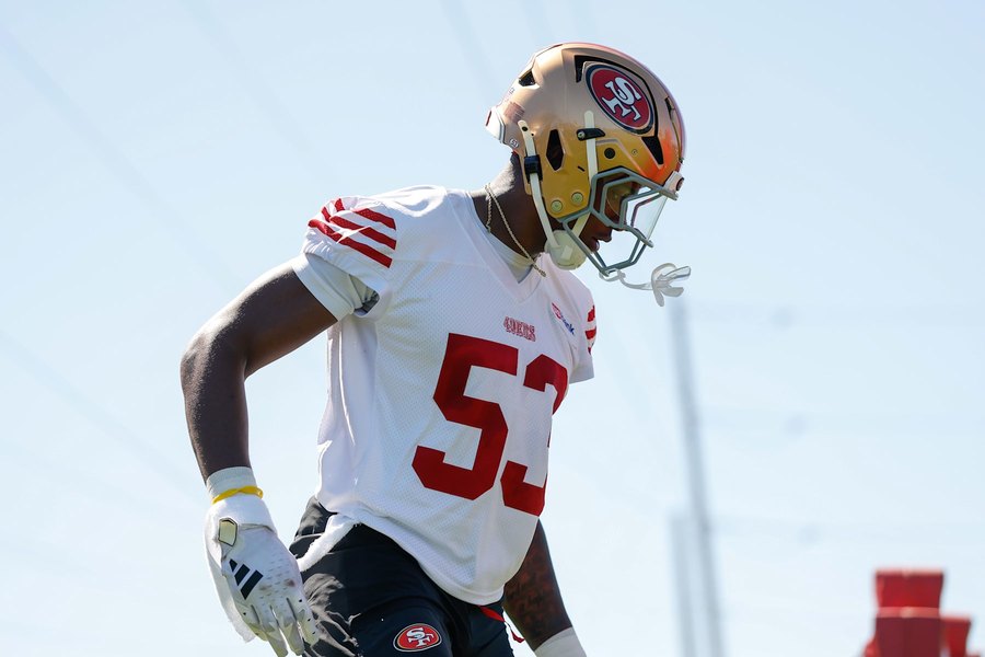 Jaden Dugger, No. 53, in a white 49ers practice jersey and gold helmet, jogging with his head turned to the field during a training camp practice in Santa Clara. A club gallery photograph, not from Las Vegas.
