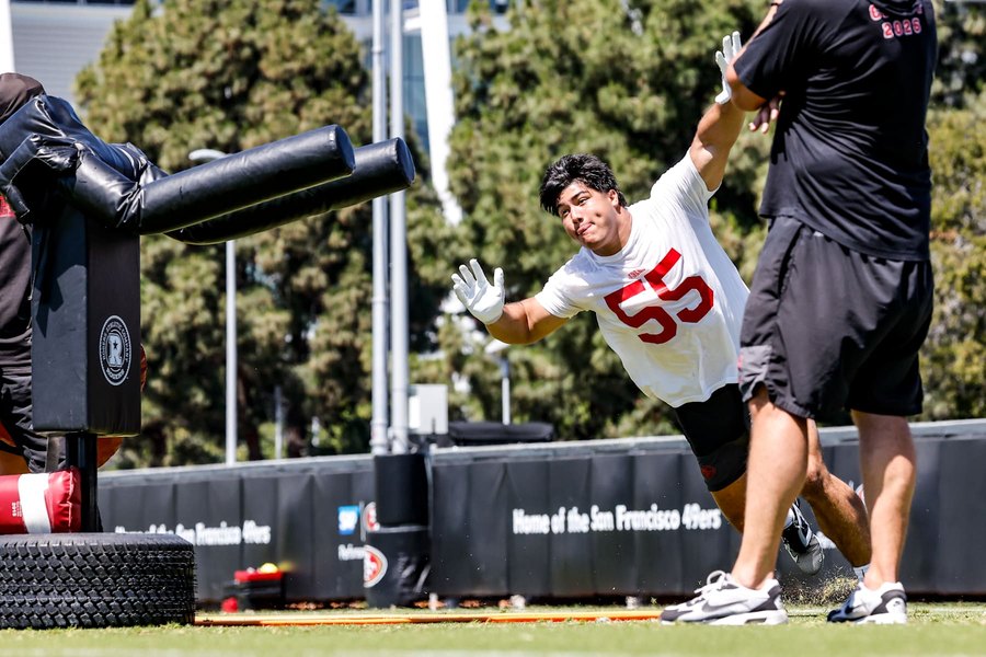 Sebastian Valdez, in a white practice jersey, dives past a blocking sled during an offseason practice at the 49ers' facility in Santa Clara.