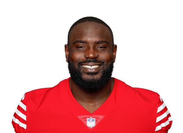 Sam Okuayinonu in a studio headshot against a white background, wearing the 49ers' scarlet home jersey with the white and gold sleeve stripes and the NFL shield at the collar, bearded and smiling.