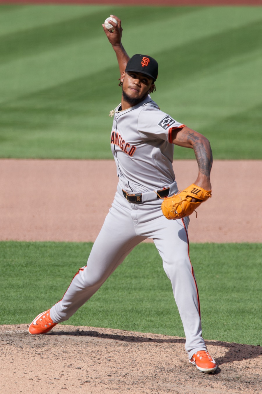 Camilo Doval in the Giants' gray road uniform and black SF cap, mid-delivery on the mound with his left leg striding forward and the ball raised behind his head. A photograph from May 2024, not from this season.