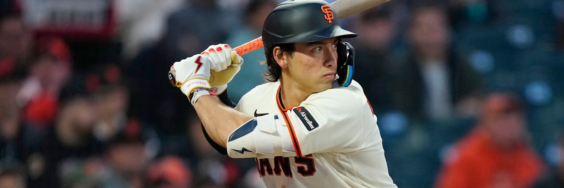 Shay Whitcomb at the plate in San Francisco's cream home uniform, the GIANTS wordmark in black and orange across his chest, bat cocked behind his right ear and a black batting helmet with the orange interlocking SF.