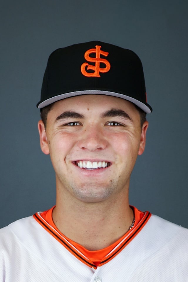 Jackson Flora in a posed head-and-shoulders portrait against a plain grey-blue background, smiling, wearing a black cap with a grey brim carrying an orange interlocking SJ and a white jersey with orange and black piping at the collar. A studio portrait in San Jose Giants uniform, not a photograph from any of the three games described here.