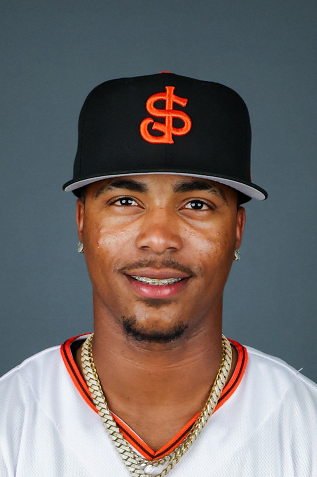 Josuar Gonzalez in the black San Jose Giants cap with the orange interlocking SJ, over a white home jersey with orange and black piping and a gold chain. It is the league's current minor league headshot for him. He is wearing braces, which is a thing you notice about a player MLB Pipeline ranks 17th in baseball.