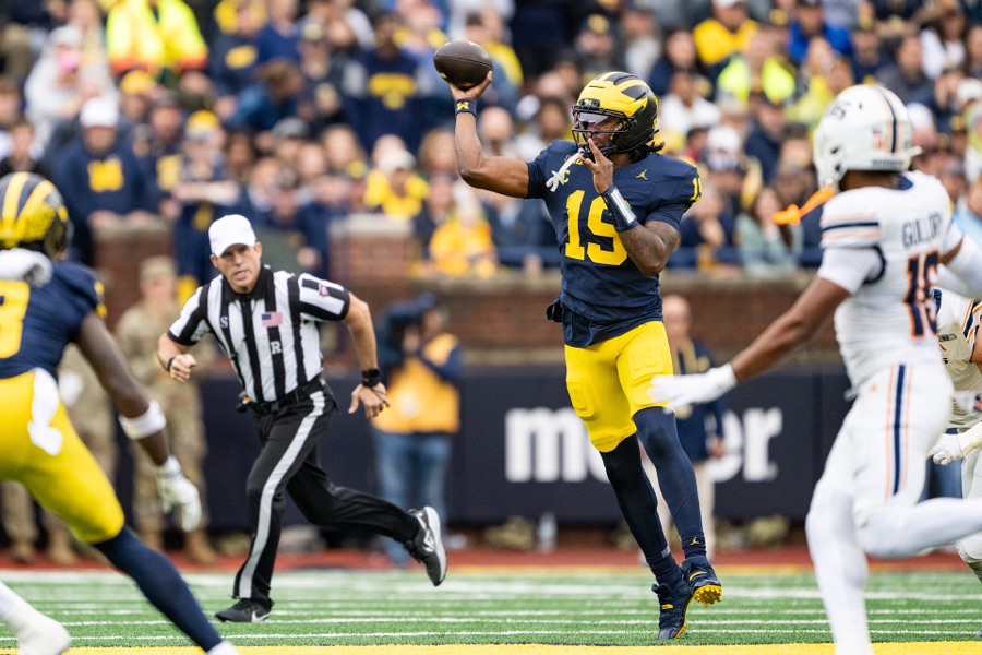 Bryce Underwood, number 19 in Michigan's navy home jersey and maize pants, throwing from the pocket against UTEP at Michigan Stadium on September 19, 2026, a UTEP defender in white closing from the right and an official trailing the play.