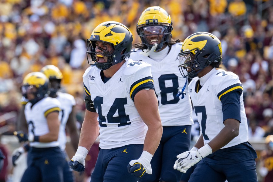 Michigan linebacker Nathaniel Staehling (44) shouts in celebration beside two teammates, all in Michigan's white road jerseys, navy trousers and winged helmets, at Huntington Bank Stadium in Minneapolis on October 3, 2026.