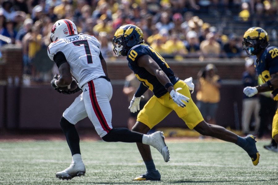 Zeke Berry, in Michigan's navy home jersey and maize pants and wearing number 10, running down an Arkansas State receiver in white and red who has just tucked the ball away, on the grass at Michigan Stadium in September 2024.