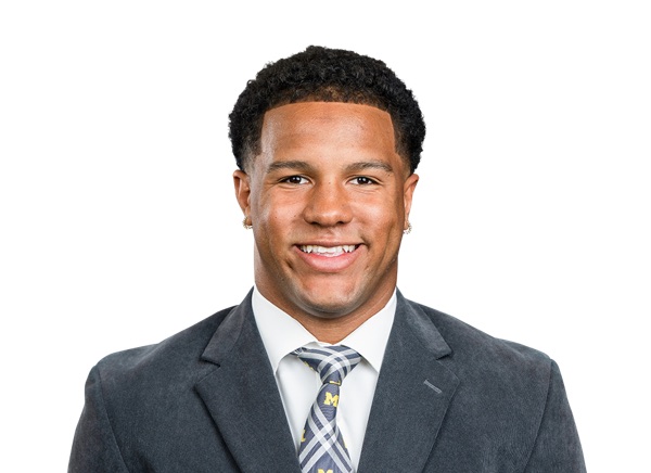 Jordan Marshall in a posed roster portrait against a white background, wearing a gray suit jacket over a white shirt and a navy and white plaid tie carrying a small maize block M. No jersey and no number are in the frame.