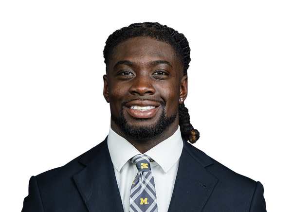 Rod Moore in a posed portrait against a white background, wearing a dark suit jacket, a white shirt and a maize and navy tie carrying a small block M. No jersey and no number are in the frame.