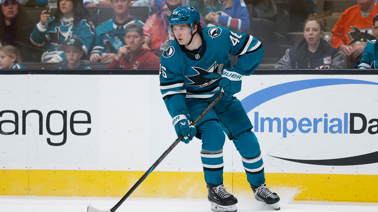 Cameron Lund in a teal San Jose Sharks sweater, head up, carrying the puck along the boards with his stick on the ice. A league photograph, undated by its source; Lund's only NHL games came in 2024-25, and he is one of the two prospects Mike Grier ruled out on the day camp opened.