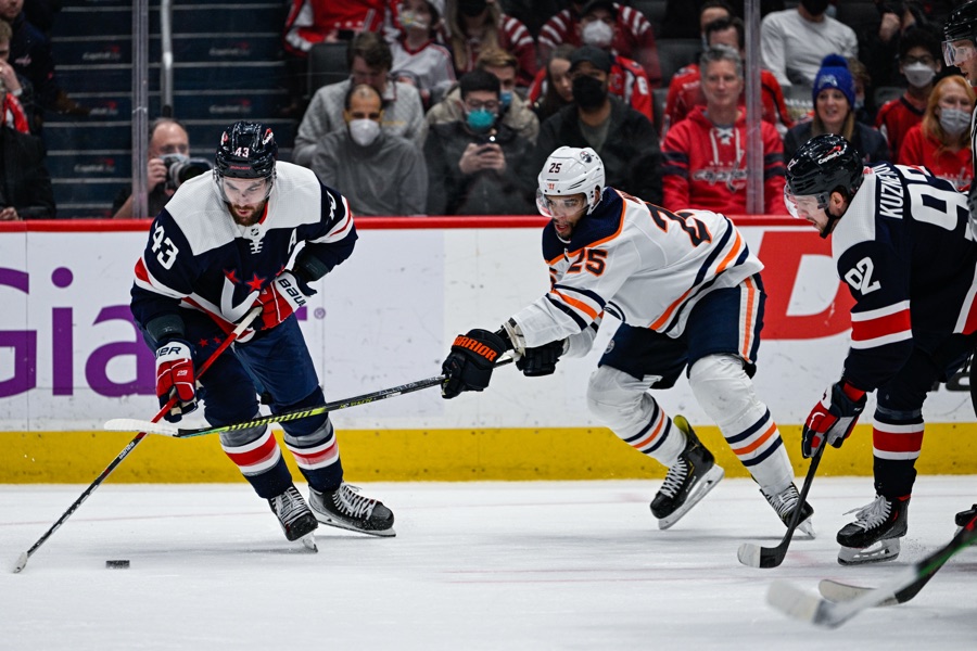 Darnell Nurse in Edmonton's white and orange away sweater, driving through two Washington defenders at Capital One Arena in February 2022. Nurse has not yet played a game for San Jose, so no picture of him in a Sharks sweater exists.