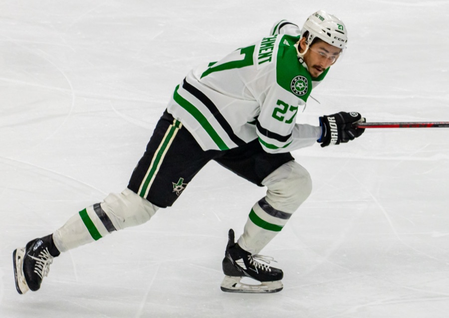 Mason Marchment in a Dallas Stars white road sweater with green and black trim, low and mid-stride with both hands on his stick, alone on clean ice.