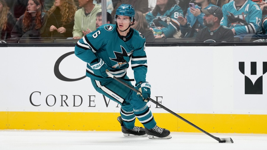 Sam Dickinson in a teal Sharks home jersey, number 6, skating the puck out of his own zone at SAP Center