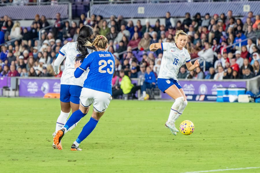Claire Hutton, in the white United States kit, plays the ball past Italy's Cecilia Salvai in Orlando in November 2025.
